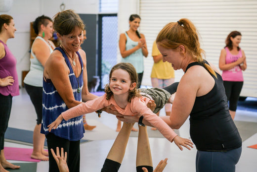 A child smiling in a supported flying pose during a joyful Rainbow Kids Yoga training activity