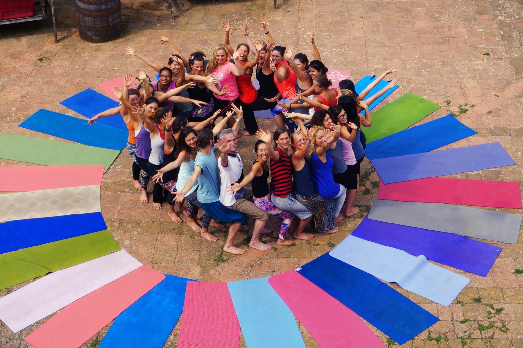 A large Rainbow Yoga group smiling together in a circle of colourful mats