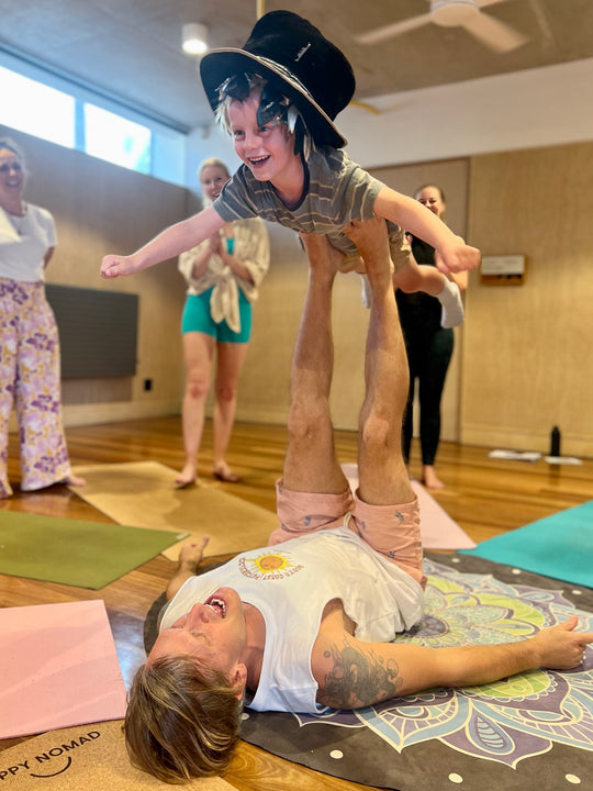 A child flying in a joyful supported Rainbow Yoga pose while the group smiles nearby