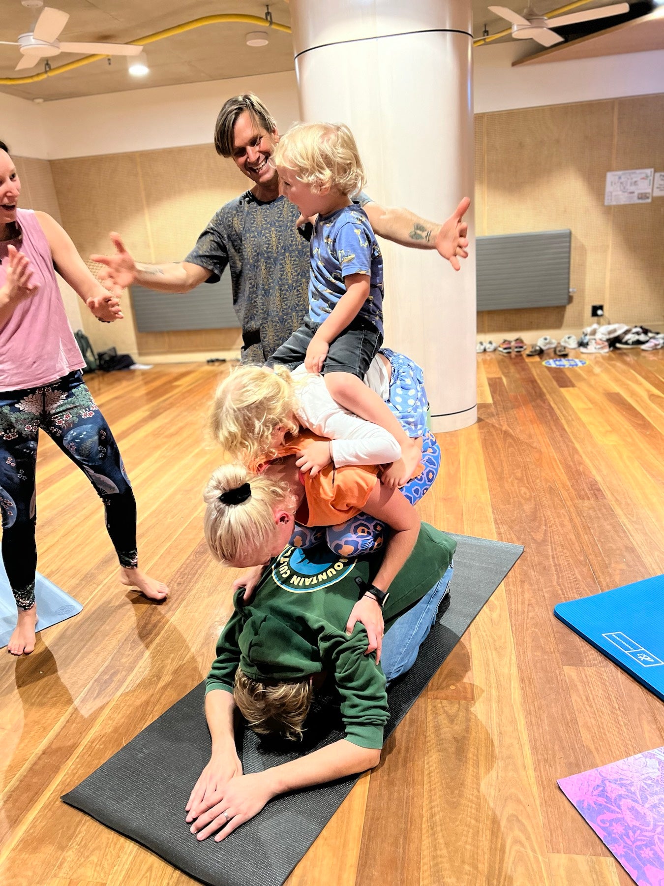 Children and adults laughing in a playful Rainbow Yoga family group shape