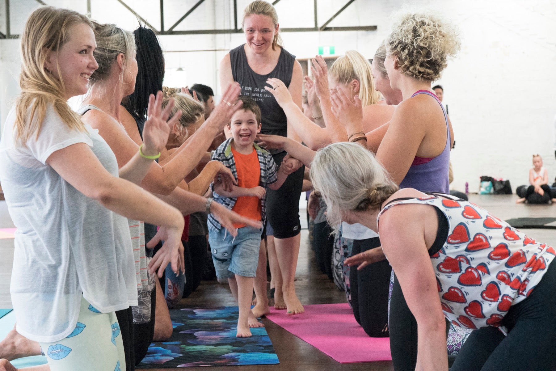 A child smiling between two lines of adults offering joyful high fives in a Rainbow Yoga class