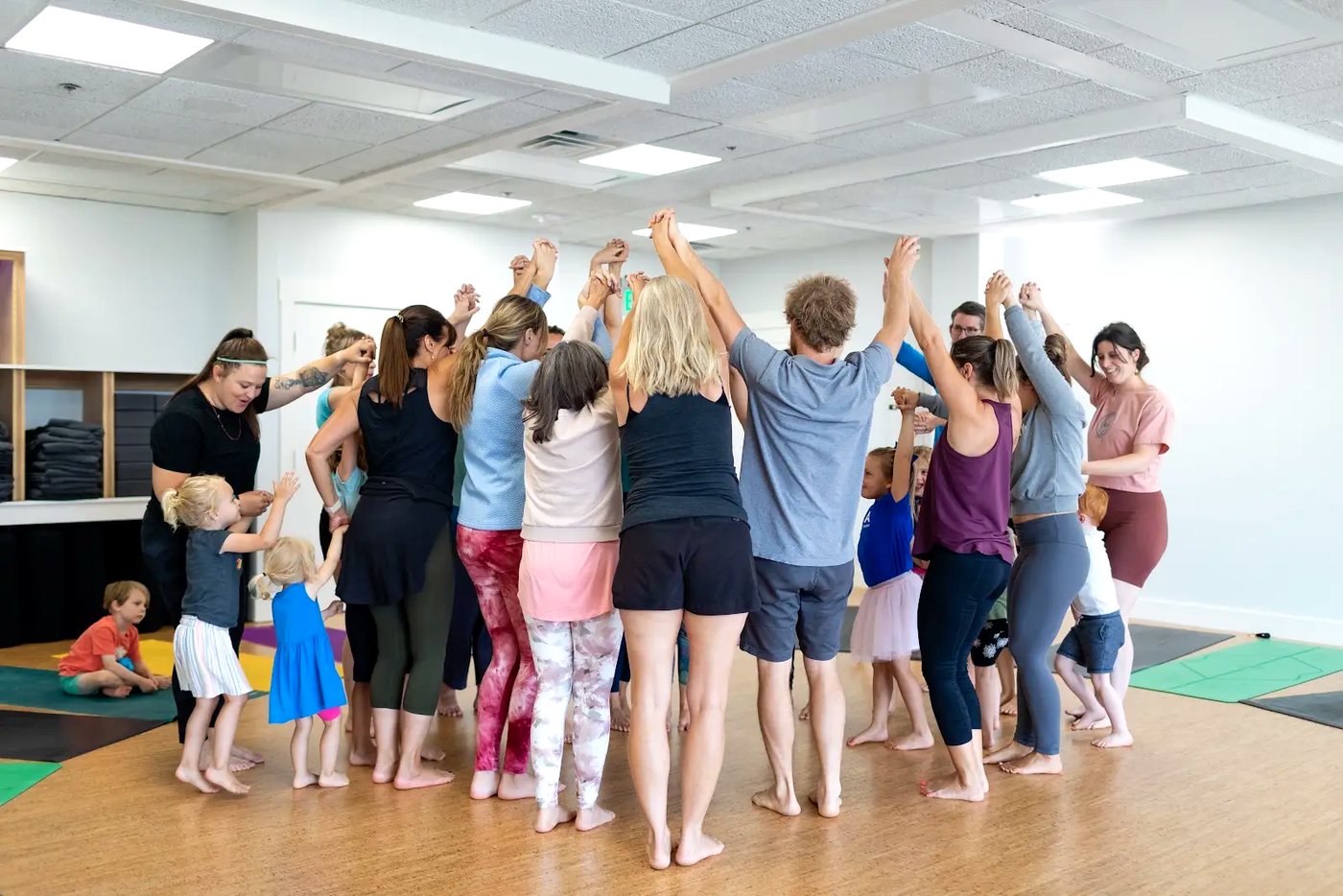 Rainbow Yoga trainees and children in a joyful circle with arms lifted