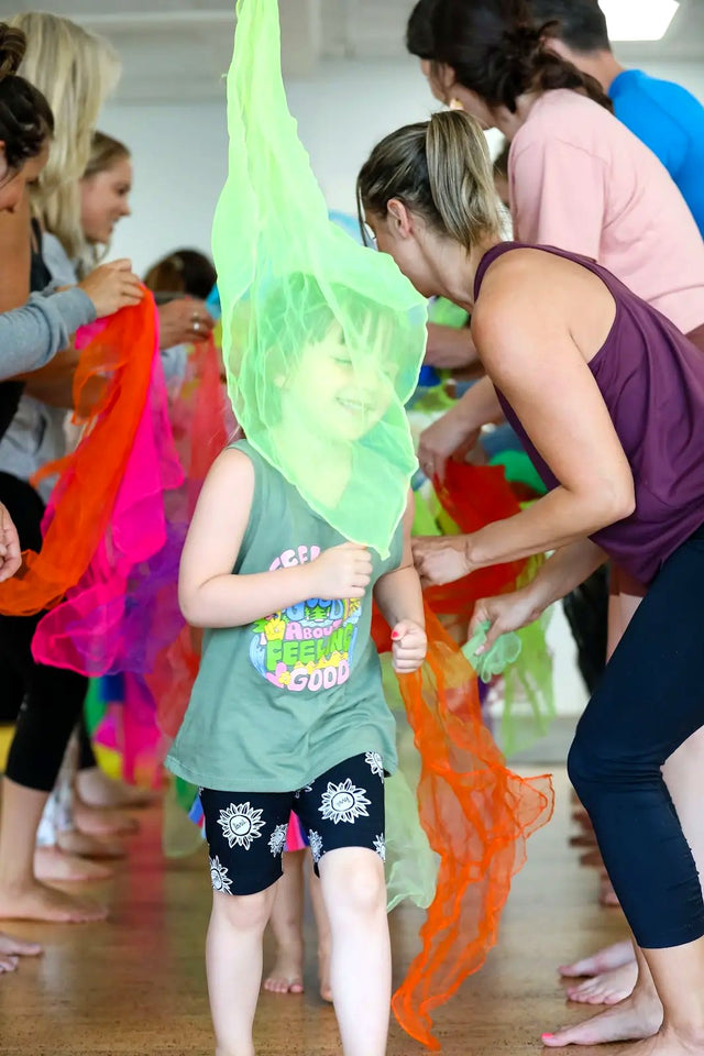 A child joyfully playing with a bright green yoga scarf