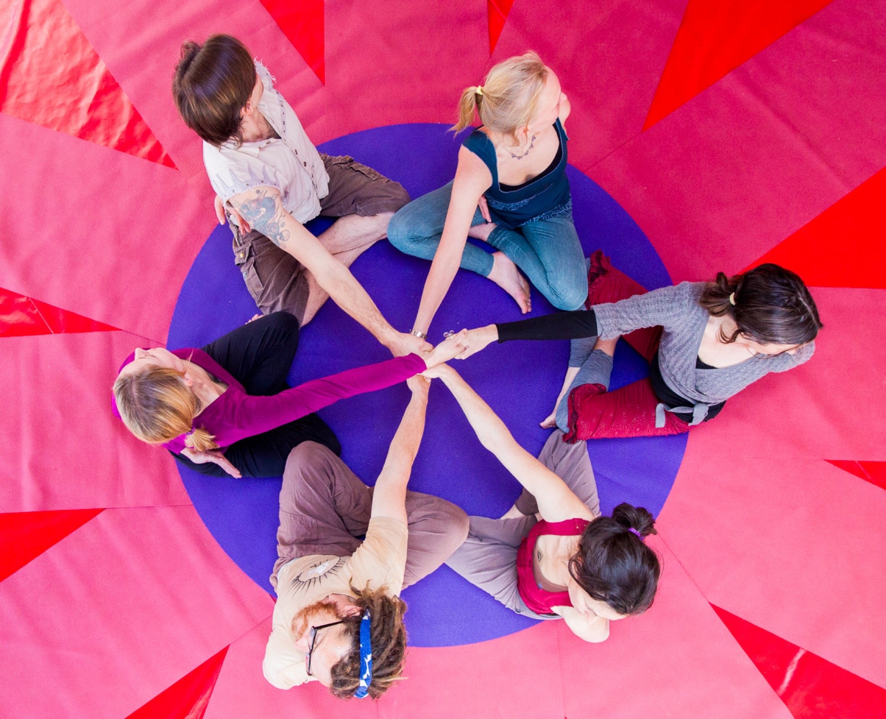 Rainbow Yoga trainees connecting hands in a bright red human mandala