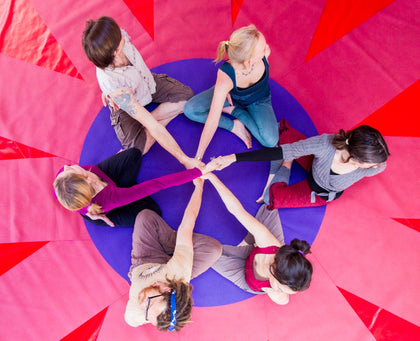 Rainbow Yoga trainees connecting hands in a bright red human mandala