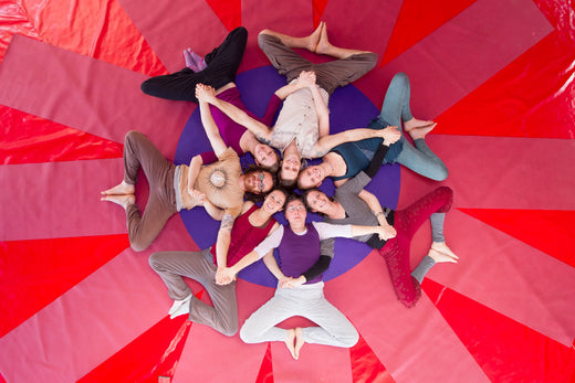 Rainbow Yoga trainees smiling in a star shape on a bright red mandala mat